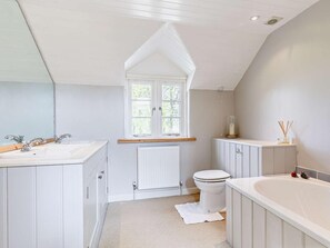 Une salle de bain avec un meuble-lavabo blanc, une baignoire, des toilettes et une fenêtre donnant sur les arbres.