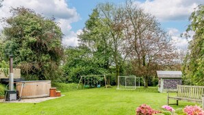 A backyard with a wooden hot tub, a swing set, a small shed, and a garden with pink flowers. - 4 Bed in Tiverton (oc-82433) (Witheridge)