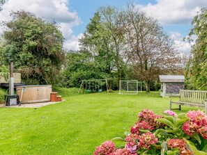A backyard with a wooden hot tub, a swing set, a small shed, and a garden with pink flowers. - 4 Bed in Tiverton (oc-82433) (Witheridge)