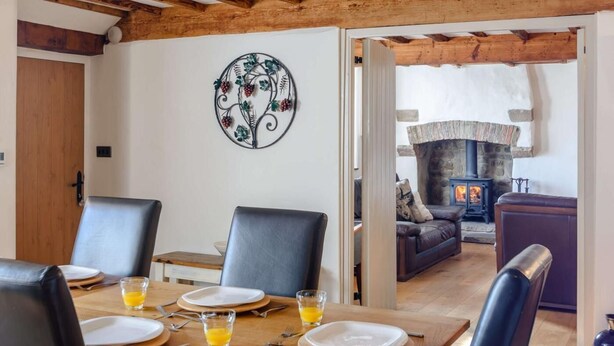 A dining area with a wooden table, chairs, and a decorative metal wall piece. - 3 Bed in Bedale (oc-81375) (Hackforth)