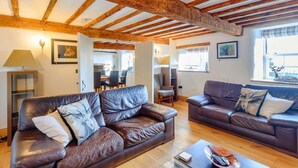 A spacious living room with leather sofas, wooden beams, a dining area, and a window with a deer outside. - 3 Bed in Bedale (oc-81375) (Hackforth)