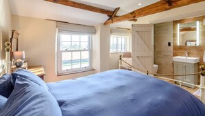 A bedroom with a large bed, a window, a bathroom with a mirror and sink, and wooden beams on the ceiling. - 3 Bed in Bedale (oc-81375) (Hackforth)
