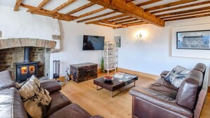 A living room with a stone fireplace, wooden beams, leather sofas, a coffee table, and a television. - 3 Bed in Bedale (oc-81375) (Hackforth)
