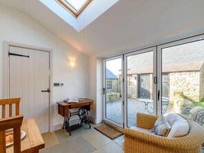 Ein Zimmer mit Oberlicht, einem Holztisch, einem Korbstuhl und einer Schiebeglastür, die zu einem Außenbereich führt.