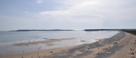 A wide beach with people walking and sitting, a calm sea, and a clear sky.