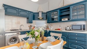 A modern kitchen with blue cabinetry, a central island with seating, and a dining table set for four. - 2 Bed in Tenby (oc-82226) (Tenby)