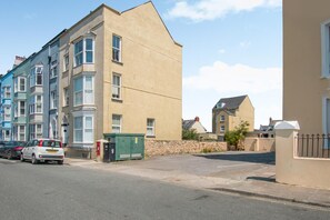 A residential street with multi-story buildings, a parked car, and a green utility box. - 2 Bed in Tenby (oc-82226) (Tenby)