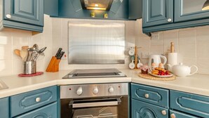 A kitchen with teal cabinets, a stainless steel range hood, a built-in oven, and a countertop with various kitchen items. - 2 Bed in Tenby (oc-82226) (Tenby)