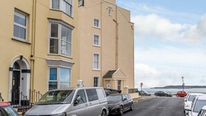 A coastal building with a bay window, a door with a black frame, and a small balcony. - 2 Bed in Tenby (oc-82226) (Tenby)