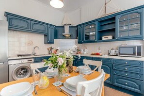 A modern kitchen with blue cabinetry, a central island with seating, and a dining table set for four. - 2 Bed in Tenby (oc-82226) (Tenby)