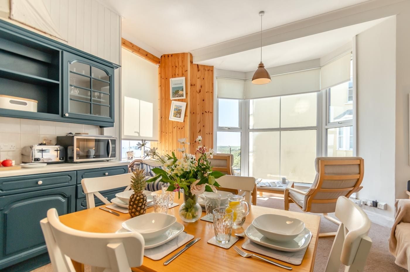 A modern kitchen with wooden accents, a dining area with a wooden table set for four, and large windows providing a view of the outdoors.