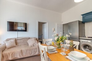 A modern living room with a sofa, a dining table set for two, and a kitchen area with a washing machine. - 2 Bed in Tenby (oc-82226) (Tenby)