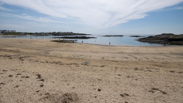 En strand med en sandstrand, lugnt vatten och klippiga utskjutande partier.