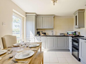 A kitchen with white cabinets, a dining table set for four, and a large window providing natural light. - 2 Bed in Holyhead (oc-81515) (Caergeiliog)