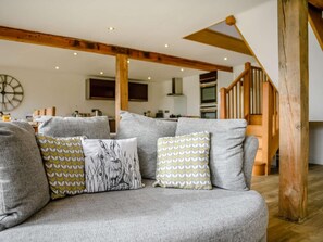 Ein Wohnzimmer mit einer Couch, gemusterten Kissen, einer Holztreppe und einer Küche im Hintergrund.