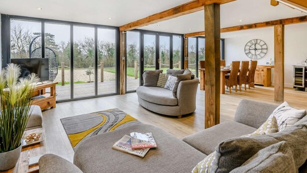 A spacious living area with a large window, a sofa, a TV, and a dining area with chairs and a table. - 2 Bed in Ipswich (oc-81441) (Witnesham)