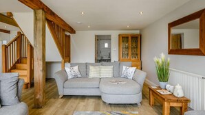 A living room with a grey sectional sofa, wooden staircase, and a cabinet with glass doors. - 2 Bed in Ipswich (oc-81441) (Witnesham)