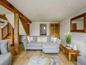 Ein Wohnzimmer mit grauem Ecksofa, einer Holztreppe und einer Vitrine.