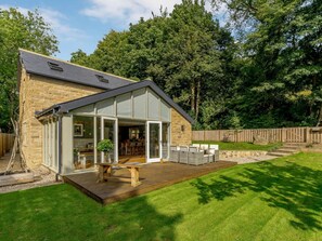 Een modern huis met een gevel van natuursteen, een grote glazen deur die leidt naar een terras voor buiten en een houten terras.