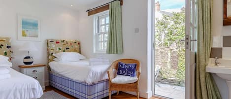 A bedroom with two beds, a chair, a window, a door, and a bathroom.