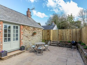 A stone house with a chimney, a wooden fence, and a patio with a table and chairs. - 2 Bed in Wadebridge (oc-82682) (Little Petherick)