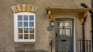 A stone building with a white window, a dark door, and a small entrance area with a doormat. - 2 Bed in Grange-over-sands (oc-82672) (Cartmel)