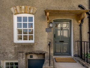 Ein Steinhaus mit einem weißen Fenster, einer dunklen Tür und einem kleinen Eingangsbereich mit Fußmatte.