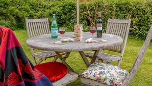Et rundt træbord med en flaske Lellegrino, et glas rødvin og en vinflaske. To træstole med blomstermønstrede hynder.