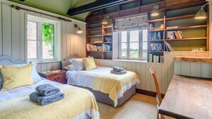 Una habitación con dos camas, una mesa de madera, una estantería y un ventanal.