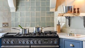 Una cocina con estufa a gas, ollas, salpicadero y un estante de madera con utensilios de cocina.