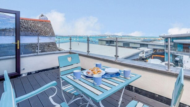 Terraza frente al mar con una mesa dispuesta para el desayuno, con vistas a un puerto deportivo y al océano.