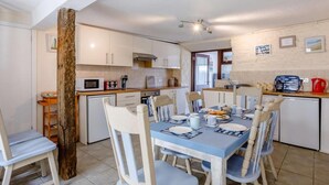 Una cocina compacta con alacenas blancas, microondas y un comedor con mesa azul y sillas blancas.