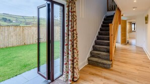 A spacious room with a large sliding glass door leading to a backyard, a carpeted staircase, and a view of the countryside. - 3 Bed in Ilfracombe (oc-82866) (Combe Martin)