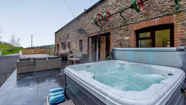 A stone building with a hot tub and outdoor seating. - 3 Bed in Ilfracombe (oc-82866) (Combe Martin)
