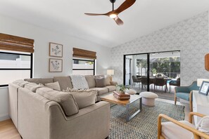A modern living room with a sectional sofa, a coffee table, and a dining area with chairs. - Renovated Naples Home l Near Vanderbilt Beach (Naples)