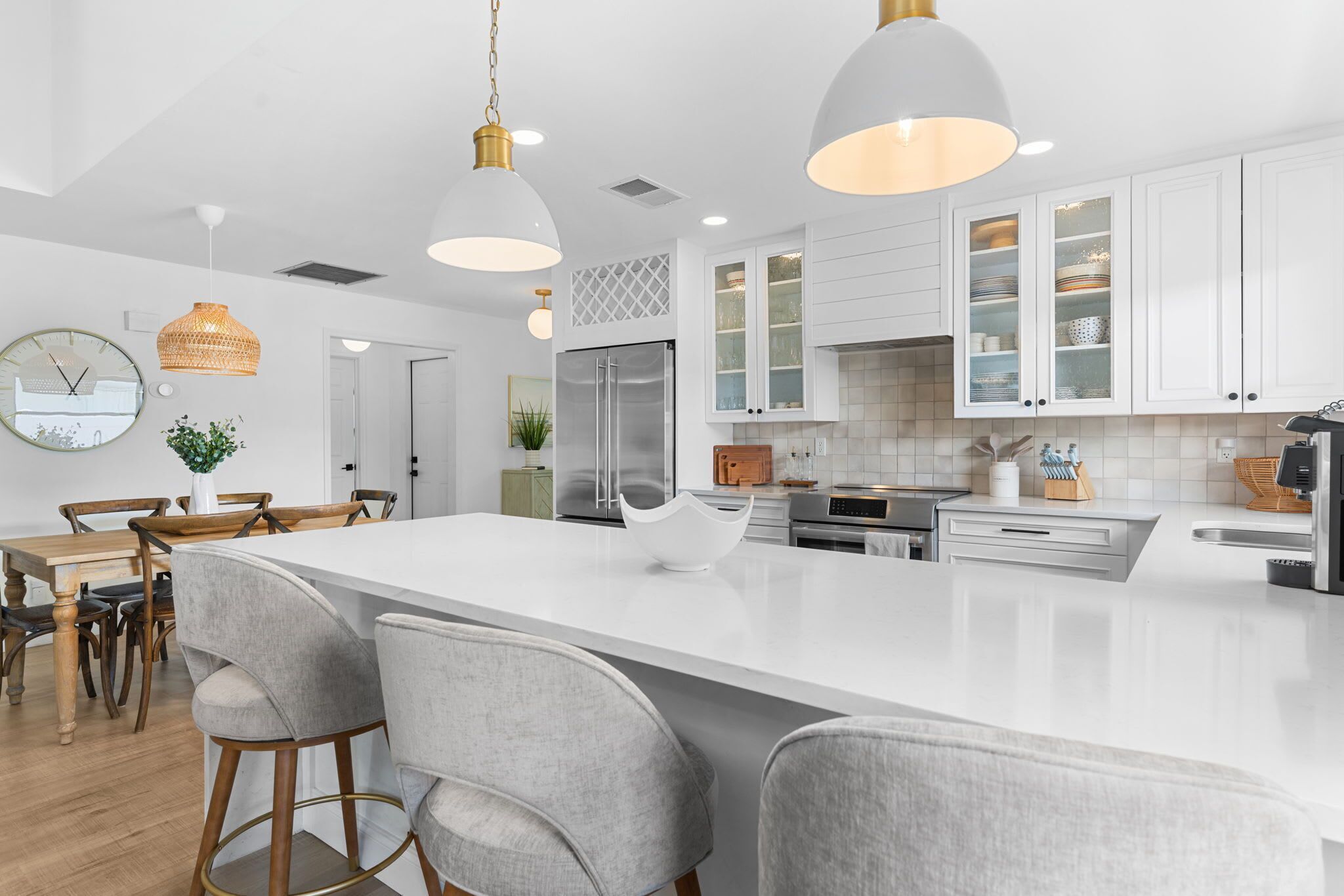Une cuisine moderne avec des meubles blancs, un grand îlot central doté de tabourets, des luminaires suspendus et un réfrigérateur en acier inoxydable.