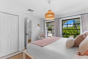 A bedroom with a bed, a window with curtains, a chair, and a hanging light fixture. - Renovated Naples Home l Near Vanderbilt Beach (Naples)