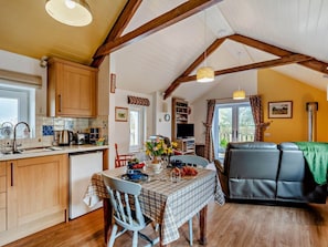 A cozy kitchen with wooden cabinets, a dining table with a checkered tablecloth, and a living area with a sofa and a television. - 2 Bed in Beaworthy (oc-82819) (Ashwater)