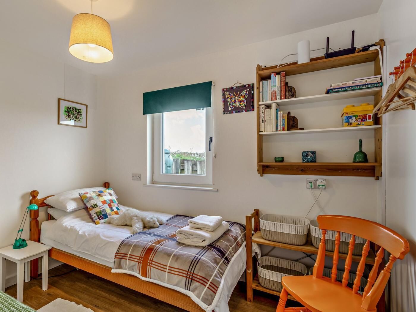Een slaapkamer met een bed, een raam, een boekenplank, een stoel en een bureau.