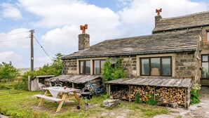 A stone house with a chimney, a wooden bench, a barbecue, and a garden with raised beds. - 3 Bed in Todmorden (oc-82953) (Todmorden)