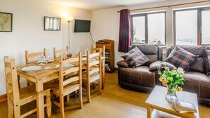 A living room with a wooden dining table, a brown leather sofa, a flat-screen TV, and a window with curtains. - 3 Bed in Todmorden (oc-82953) (Todmorden)