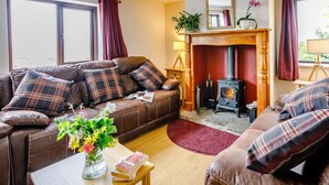 A living room with a sofa, a small table with a vase and book, a fireplace, and a window with curtains. - 3 Bed in Todmorden (oc-82953) (Todmorden)