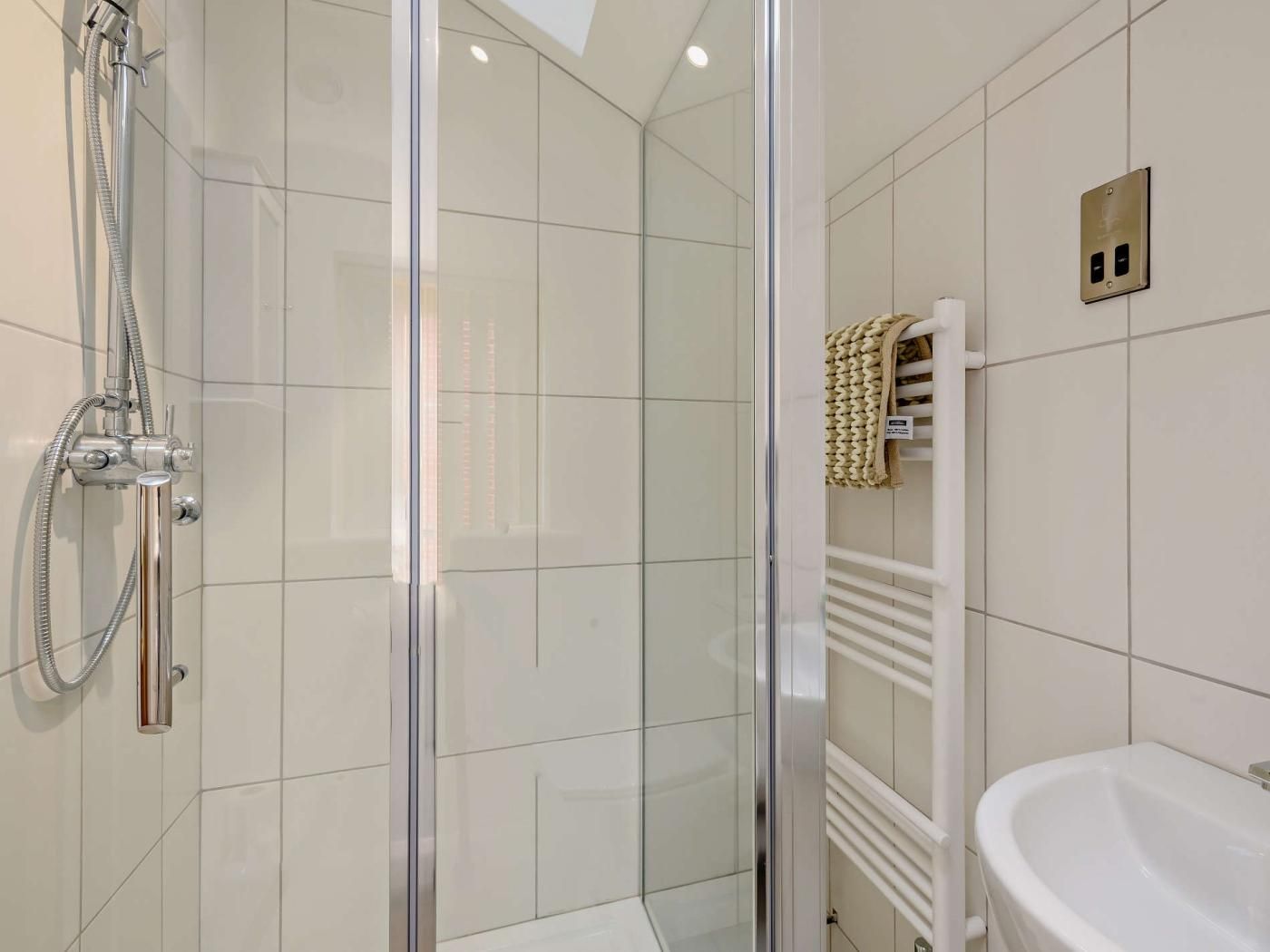 Ein modernes Badezimmer mit Duschkabine aus Glas, einem weißen Waschbecken und einem Handtuchhalter.
