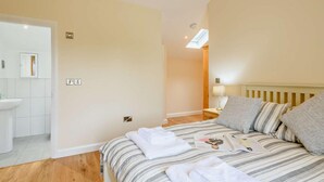 Ein Schlafzimmer mit Bett, Nachttisch, Lampe und einem Badezimmer mit Waschbecken und Spiegel.
