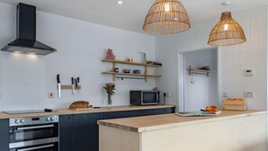 Ett modernt kök med en central köksö, inbyggd ugn, mikrovågsugn och upphängda köksredskap.