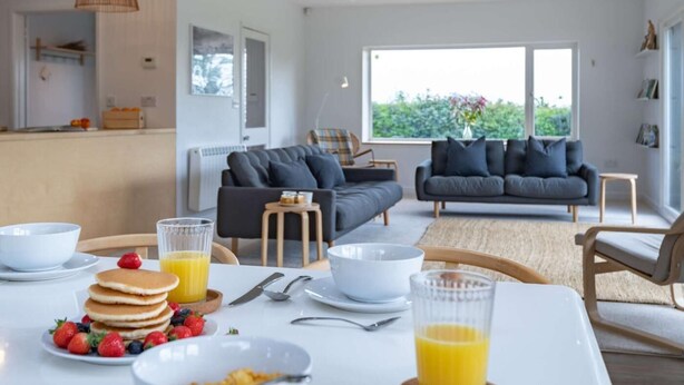 Ett modernt vardagsrum med en soffa, ett matbord med frukost på och ett stort fönster.