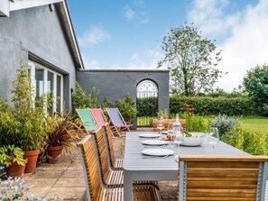 An outdoor patio with a dining table set for four, surrounded by wooden chairs and a bench. - 4 Bed in Melton Constable (oc-83070) (Sharrington)