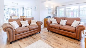 A spacious living area with two brown leather sofas, a wooden coffee table, and a large window providing a view of the outside. - 3 Bed in Torquay (oc-82959) (Torquay)
