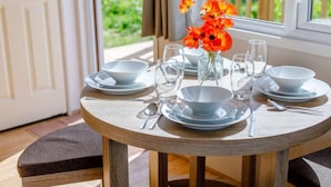 A round wooden table set for dining with white plates, bowls, and cutlery, and a vase with orange flowers. - 2 Bed in South Brent (oc-82871) (South Brent)