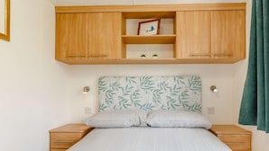A bedroom with a bed, wooden cabinets above, and a wall-mounted shelf with a picture. - 2 Bed in South Brent (oc-82871) (South Brent)